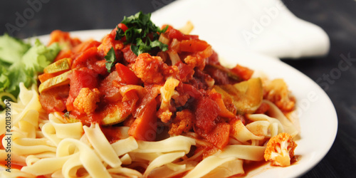 Ribbon pasta with Arrabiata sauce. Close up. Mediterranean dish. Tagliolini pasta with vegetables. Cauliflower, courgette and tomato stew. Italian cuisine. Vegan and vegetarian. Wide photo.