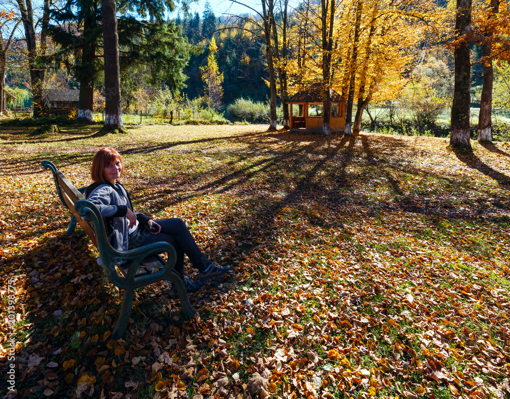 Woman on bench in autumn Carpathian mountain sunny park on river shore. Woman on bench in autumn Carpathian mountain sunny park on river shore.