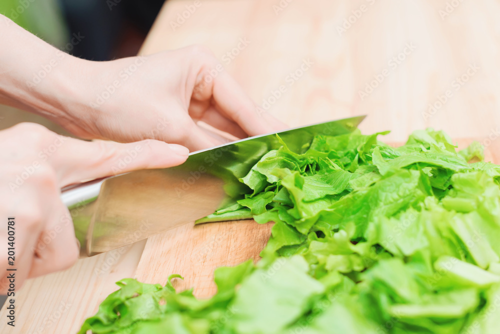 Close-up Female hands chopping a green plant salad cooking salad from vegetables on a wooden cutting board at home. The concept of vegetarianism and healthy lifestyles Close-up Female hands chopping a green plant salad cooking salad from vegetables on a wooden cutting board at home. The concept of vegetarianism and healthy lifestyles