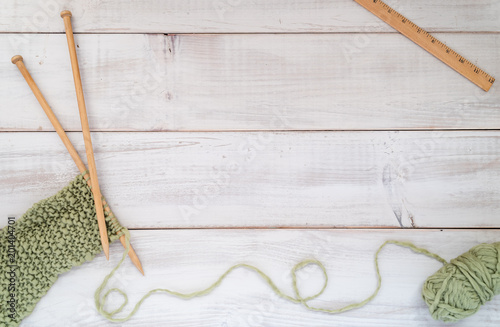 Knitting needles, yarn and ruler on a whitewashed wood table