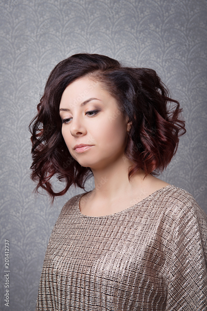 A brown-haired woman with a stylish hairstyle and clean skin looking down on a gray background close-up. A brown-haired woman with a stylish hairstyle and clean skin looking down on a gray background close-up.