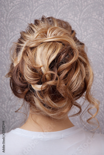 Hairstyle bunch on the basis of the curls on blonde head rear view on gray vintage background. Professional women's hairstyle.