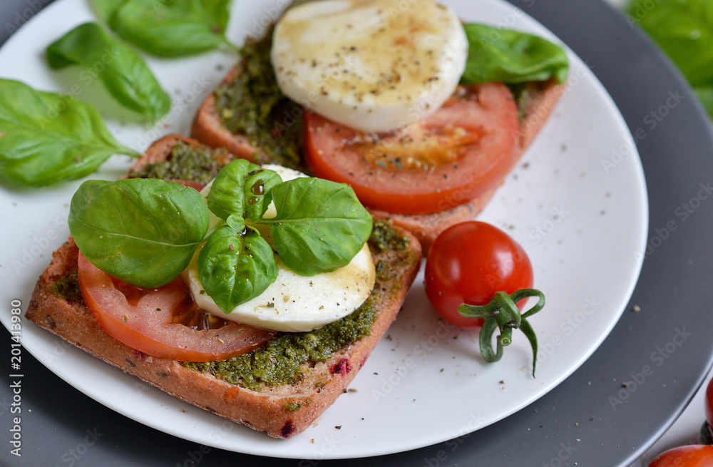 Sandwich with mozzarella cheese and red tomatoes, basil leaves, pepper, olive oil, gray plate, healthy breakfast, food concept, white background