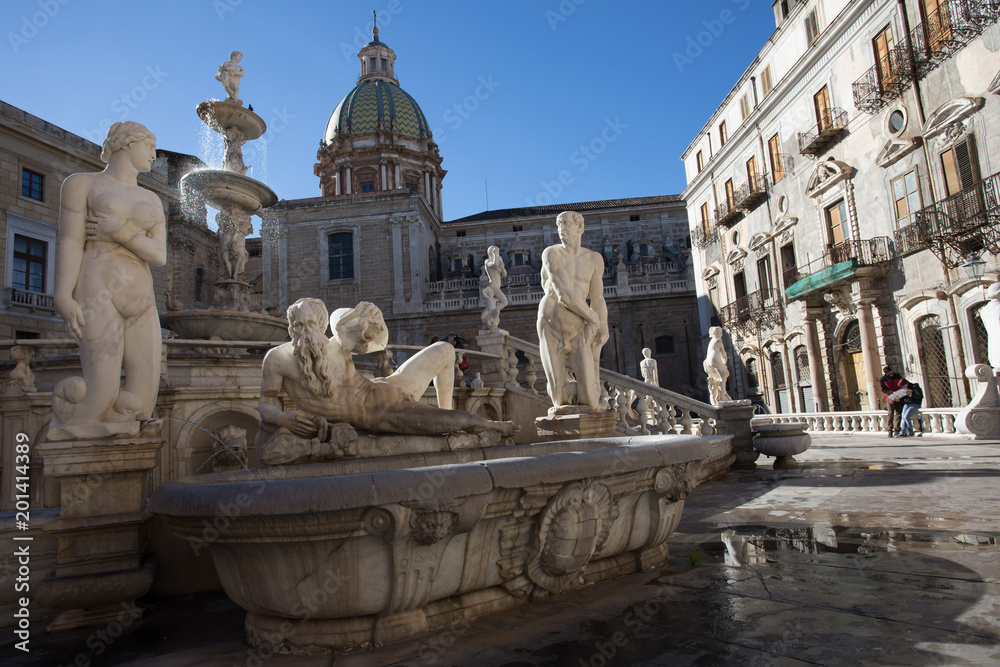 Pretoria Fountain, Palermo. Group of white marble statues part of the Pretoria Fountain of Palermo. Statues of naked woman and man, and Poseidon laying down. With church dome at background.