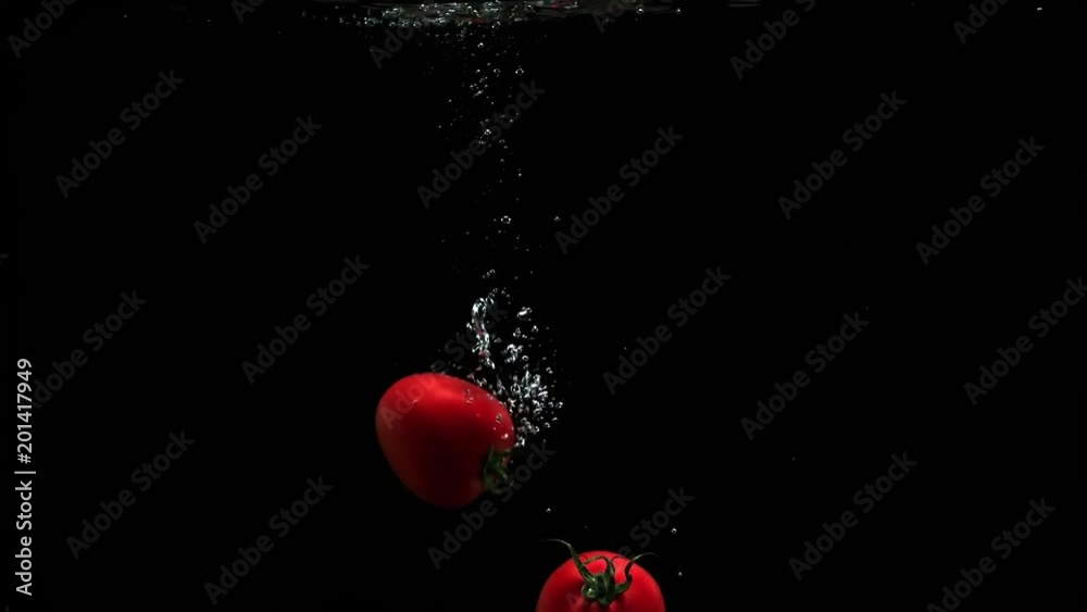 Fresh ripe tomatoes falling into clean water with air bubbles and droplets on black background Fresh ripe tomatoes falling into clean water with air bubbles and droplets on black background