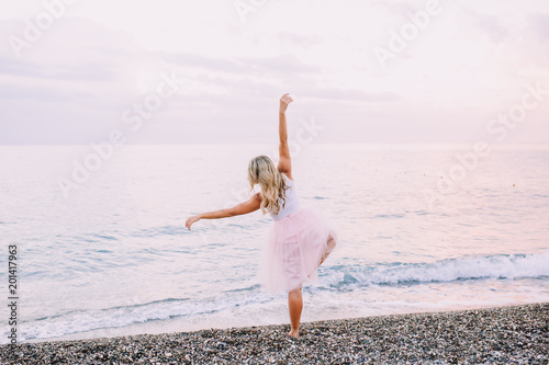 Blond girl is dancing on the beach at sunrise