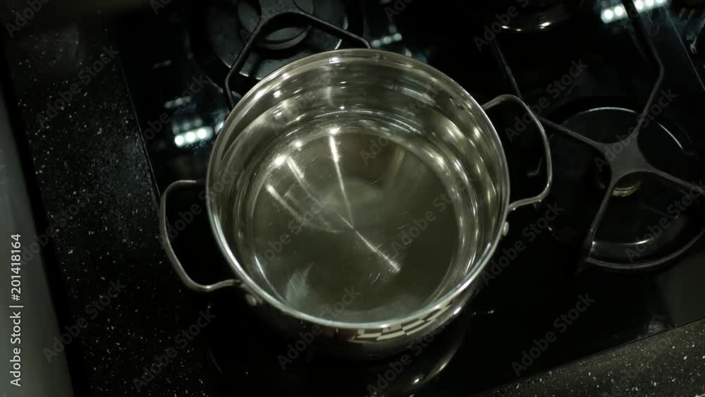 The chrome pot with water is on the black gas stove. The gas is switched on. The chrome pot with water is on the black gas stove. The gas is switched on.