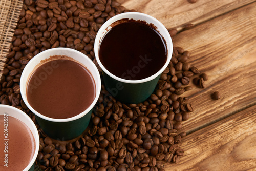 Three take away green paper cups with coffee beans and hot chocolate drink on wooden background  top view  close-up