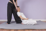 Young woman lying while enjoying stretching and the acupressure techniques of traditional Thai massage at spa and wellness center