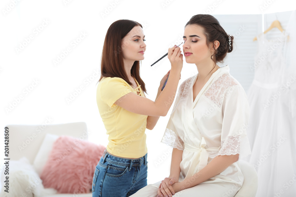 Professional makeup artist working with young bride in salon
