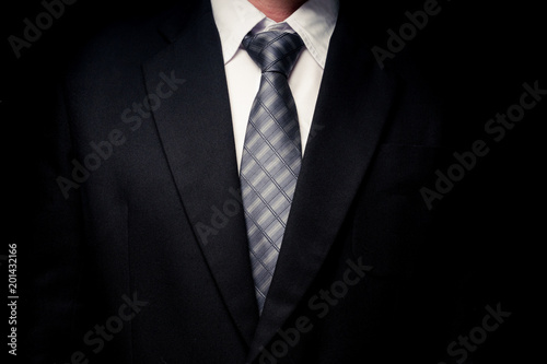 Close up of man in black suit, shirt and tie on black background