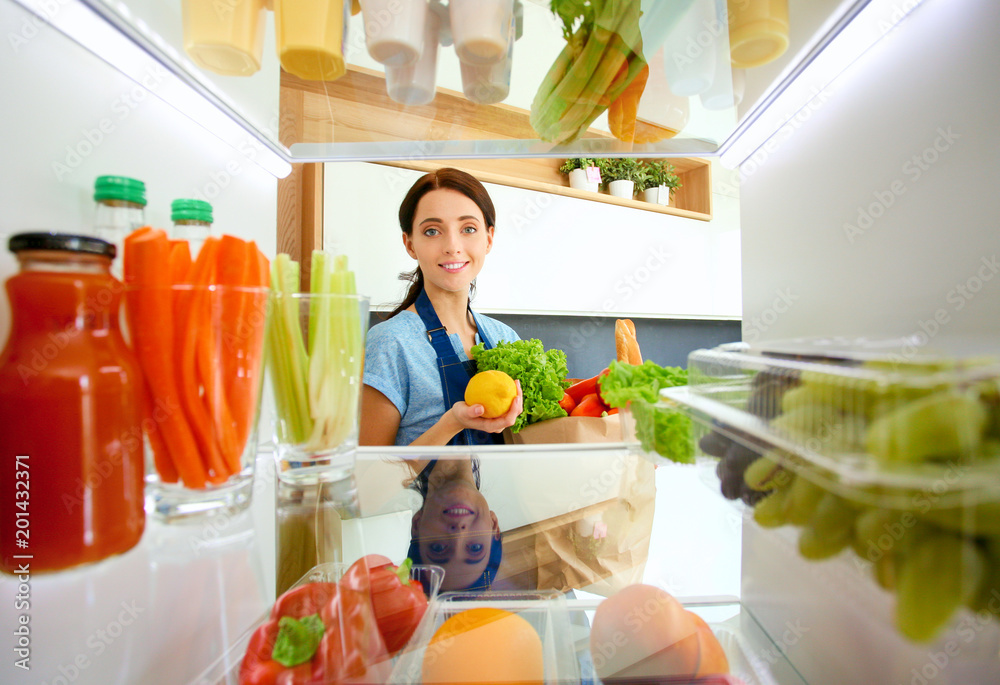 Portrait of female standing near open fridge full of healthy food, vegetables and fruits. Portrait of female