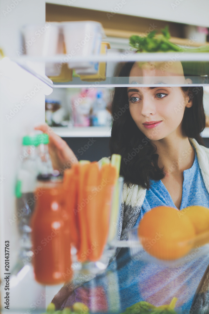 Portrait of female standing near open fridge full of healthy food, vegetables and fruits. Portrait of female