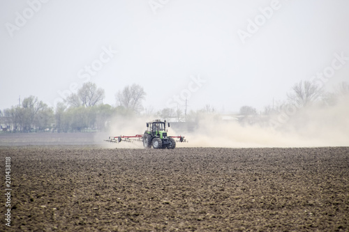 The tractor harrows the soil on the field and creates a cloud of dust behind it © eleonimages