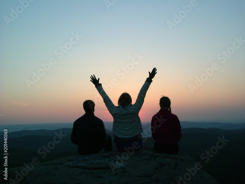 Three friends sit on top of the mountain and enjoy the sunset.