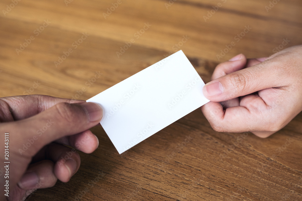 Businessman giving an empty business card to businesswoman on wooden table background Businessman giving an empty business card to businesswoman on wooden table background