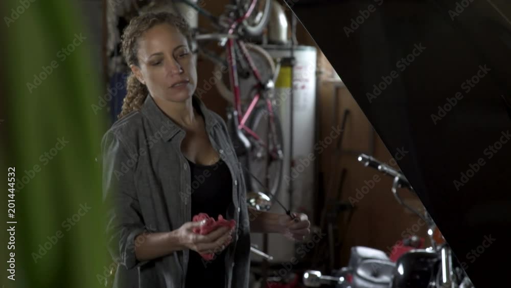 Mature woman measuring oil with dipstick in car engine and smiling.