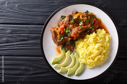 Portion of seco de chivo stewed goat meat with yellow rice and avocado close-up on a plate. Horizontal top view photo