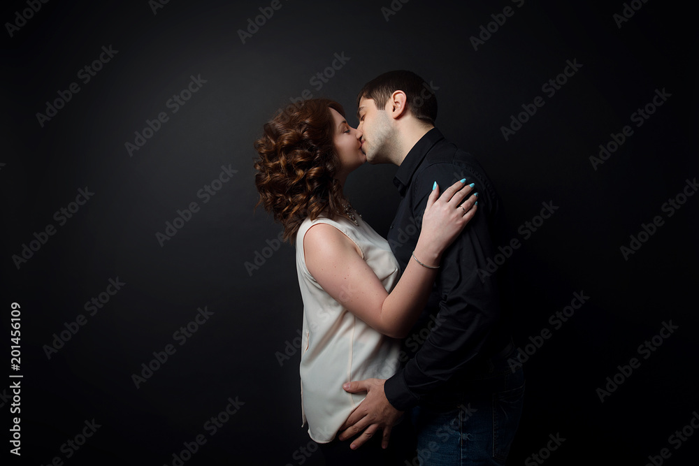 A loving couple kisses against a black isolate. A loving couple kisses against a black isolate.