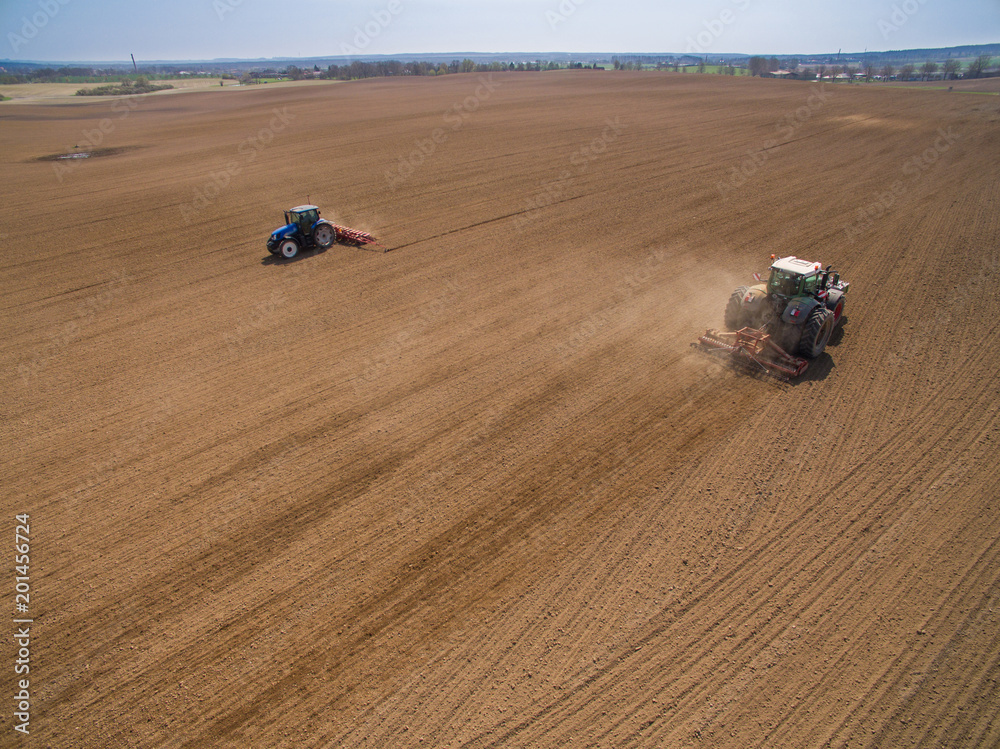 aerial view - two tractors working on the agricultural field plowing and sowing in the field 