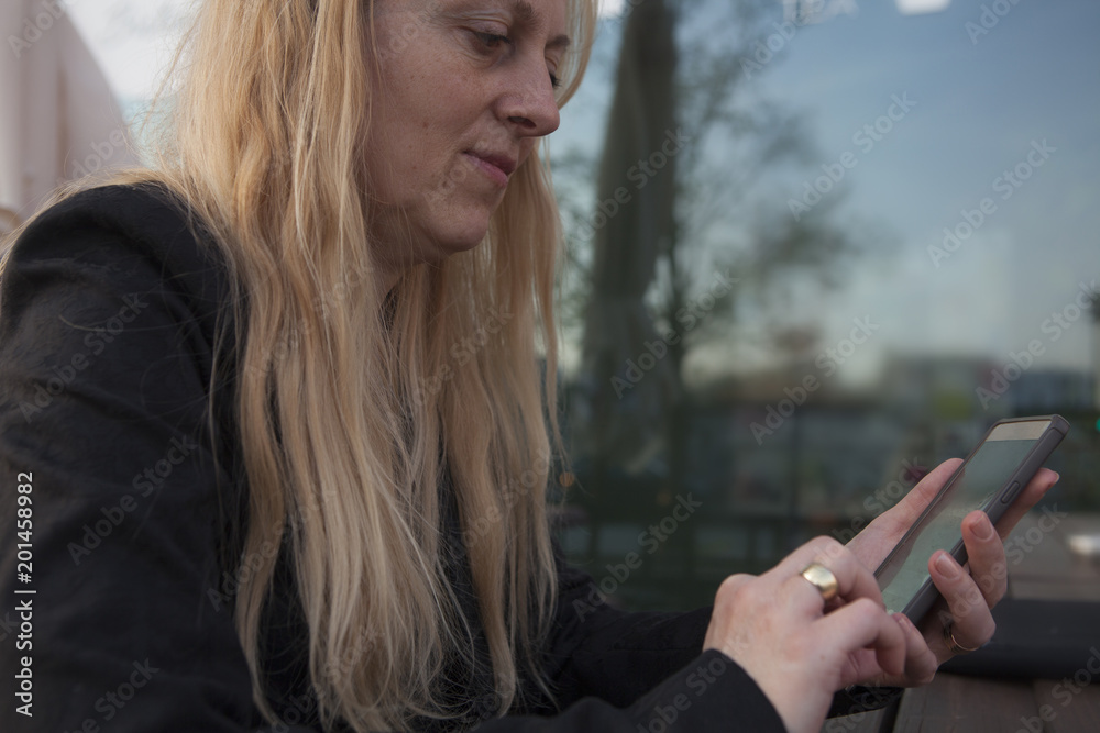 Mujer de negocios sentada en el exterior concentrada consultando su teléfono móvil.