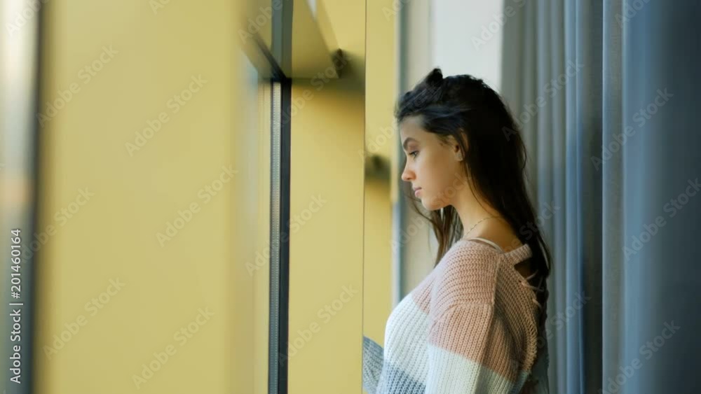 young pensive beautiful girl. home leisure pastime. standing at the window looking out as if waiting young pensive beautiful girl. home leisure pastime. standing at the window looking out as if waiting