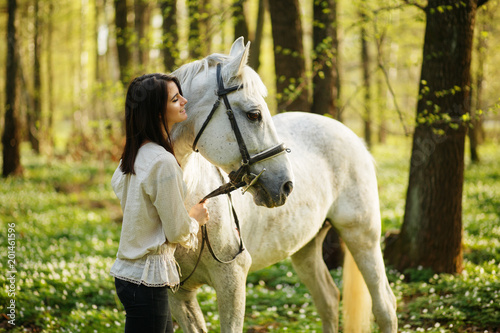 Woman with a white horse in the spring foresn. Anemone flower in the forest in the sunny day. Wood anemone, windflower