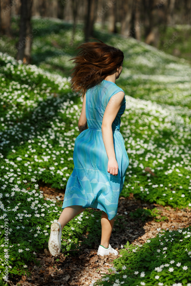 Woman runs through the forest in a long dress. Relaxing woman at nature. Happy pretty young woman enjoying smell flowers over spring forest background Woman runs through the forest in a long dress. Relaxing woman at nature. Happy pretty young woman enjoying smell flowers over spring forest background