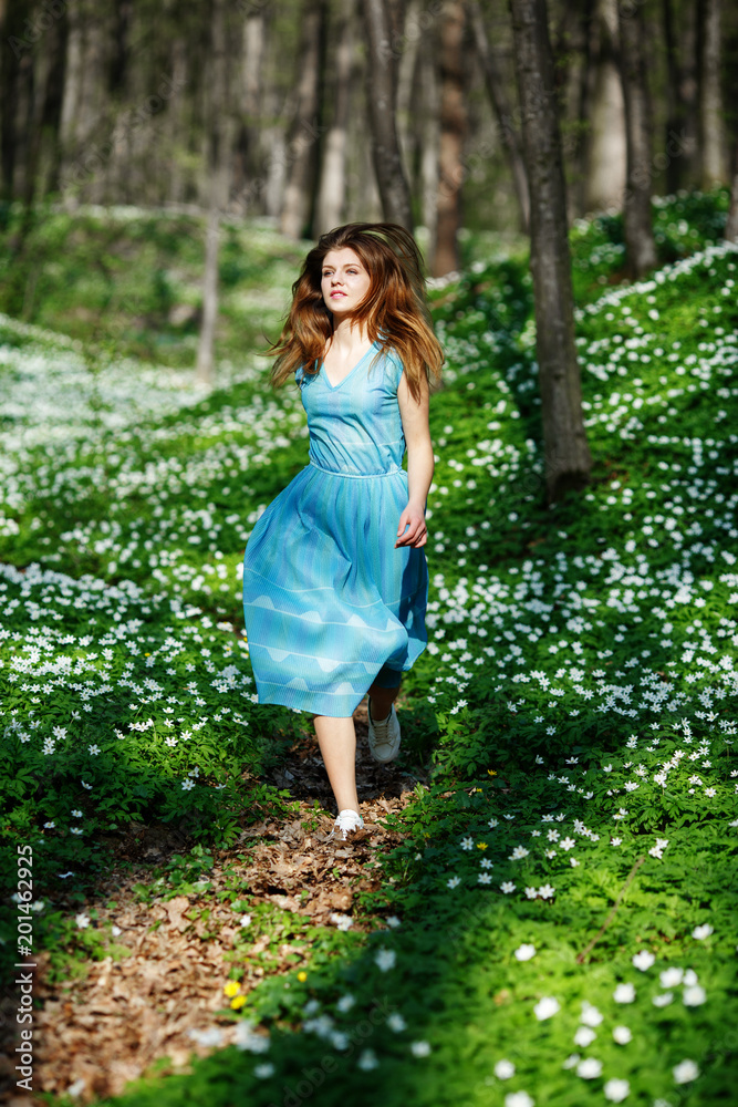 Woman runs through the forest in a long dress. Relaxing woman at nature. Happy pretty young woman enjoying smell flowers over spring forest background