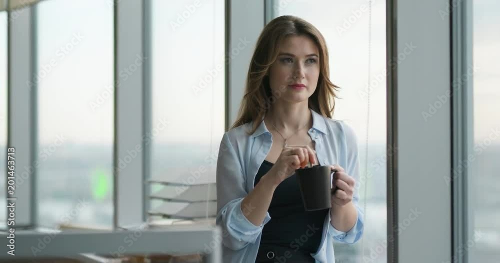 A woman in the office by the window with cup A woman in the office by the window with cup