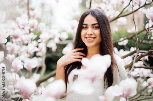 Young pretty woman portrait near flower of blossom magnolia tree. Spring time