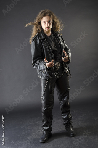 Full length portrait of a cool attitude metalhead, wearing leather clothing with stude, long hair and beard. Background is black photo