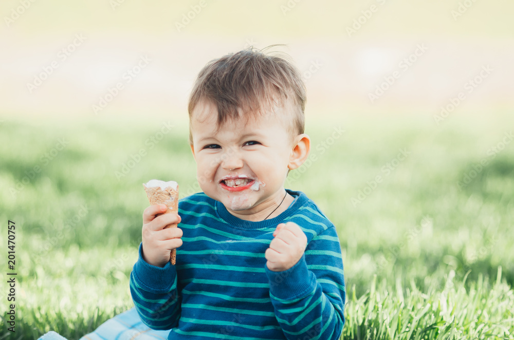 Cheerful child in a blue sweater eating ice cream on a background of grass, outdoors