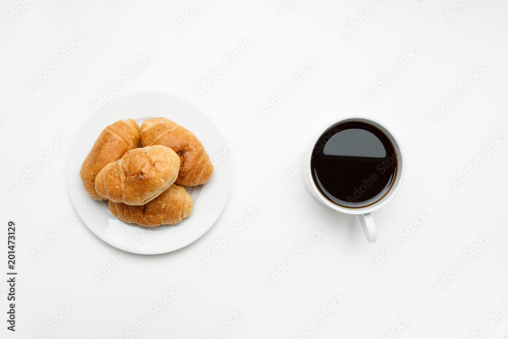 Fresh croissant in a white plate and cup of coffee, top view
