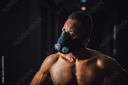 african american man in mask looking at camera with angry sight close-up in gym. black men and black background