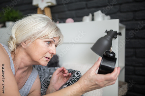 Senior woman holding alarm clock checking out time