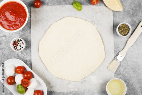 Pizza dough and ingredients for pizza on gray background. Top view. Food background