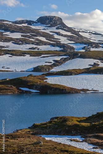 Majestic view of a mountain plateau Hardangervidda with snow mounts and river in summer time, Norway national park