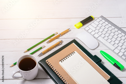 Wooden White office desk table with cup of coffee, Notebook, Pen, Marker on it.