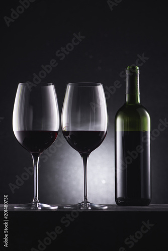 glasses filled with red wine and wine bottle on black