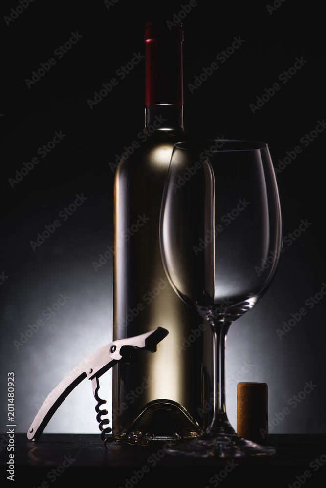 bottle of white wine with corkscrew and wineglass on black