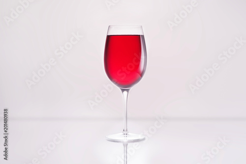 glass full of red wine on reflective surface and on white