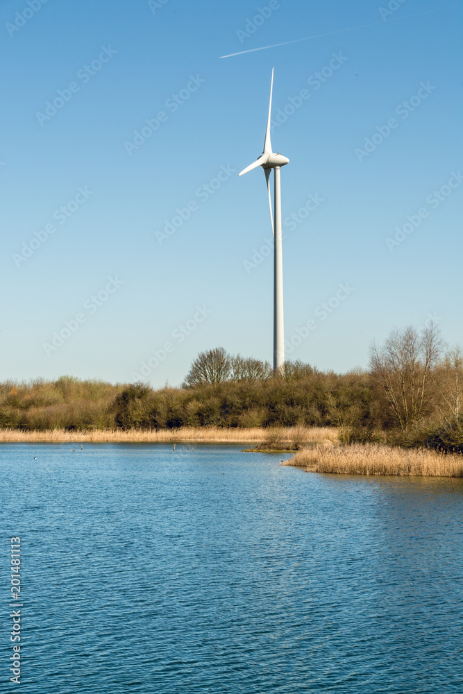 Blue water in the lake and a windmill on the lakeside on sunny day - environmental nature background - vertical Blue water in the lake and a windmill on the lakeside on sunny day - environmental nature background - vertical