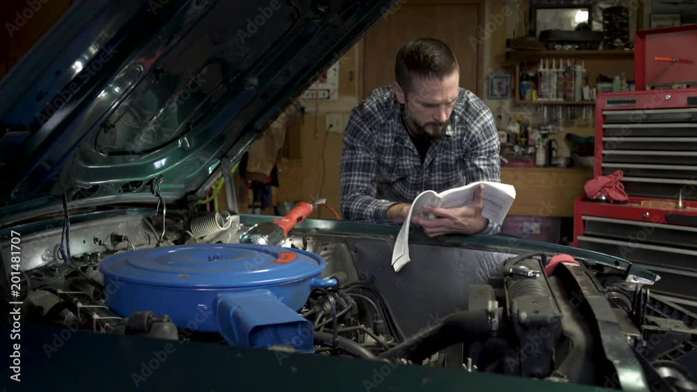 Mature man referring to car instruction manual by open car bonnet. Mature man referring to car instruction manual by open car bonnet.