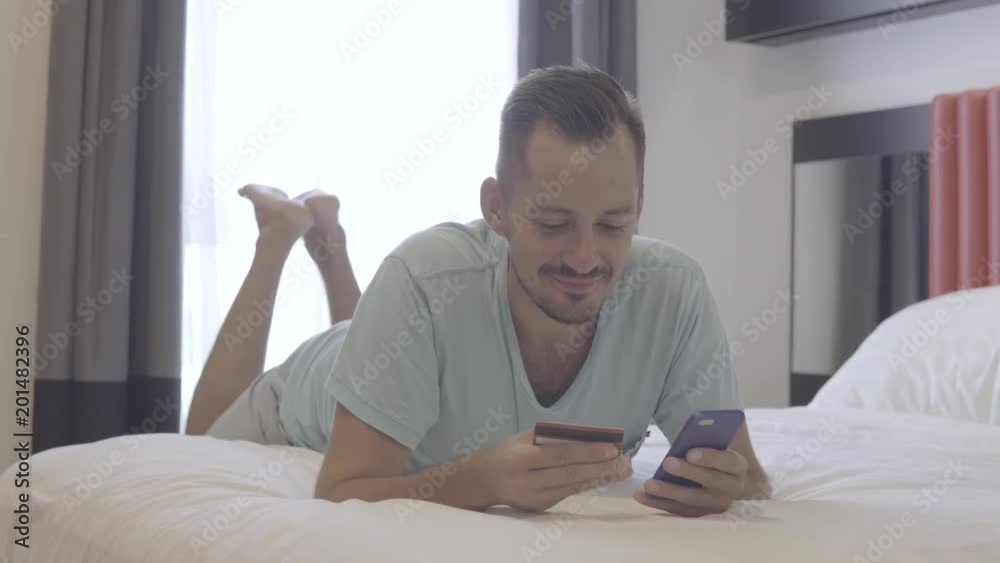 Man made successful payment with credit card and smartphone, lie on the bed. Man made successful payment with credit card and smartphone, lie on the bed.