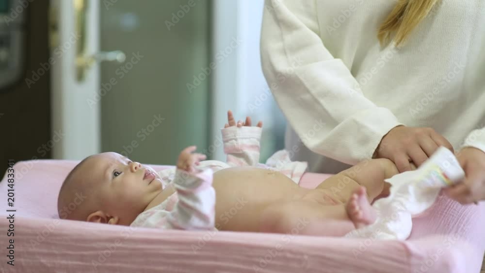 Mother changing baby daughter's nappy, panning left, surface level.