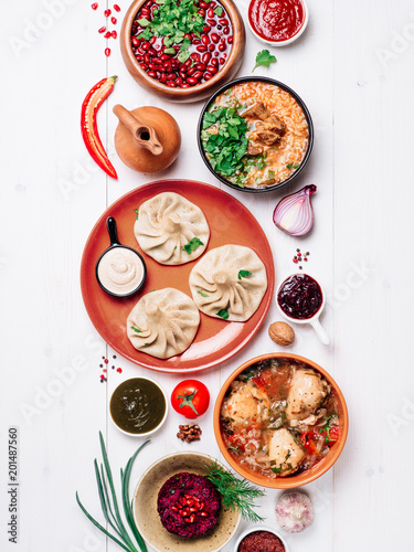 View from above of georgian cuisine on white wooden table. Traditional georgian food - khinkali, kharcho, chahokhbili, phali, lobio and local sauces - tkemali, satsebeli, adzhika. Top view. Vertical. photo