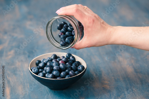Woman putting freshly gathered blueberries from a jar into a small bowl