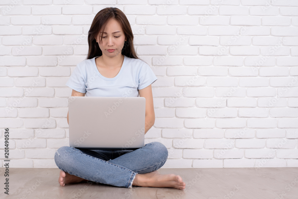Beautiful young woman in casual wear is using a laptop and smiling, sitting against white brick wall. Portrait of young asian woman working and using laptop computer outdoor on isolated bric. Beautiful young woman in casual wear is using a laptop and smiling, sitting against white brick wall. Portrait of young asian woman working and using laptop computer outdoor on isolated bric.