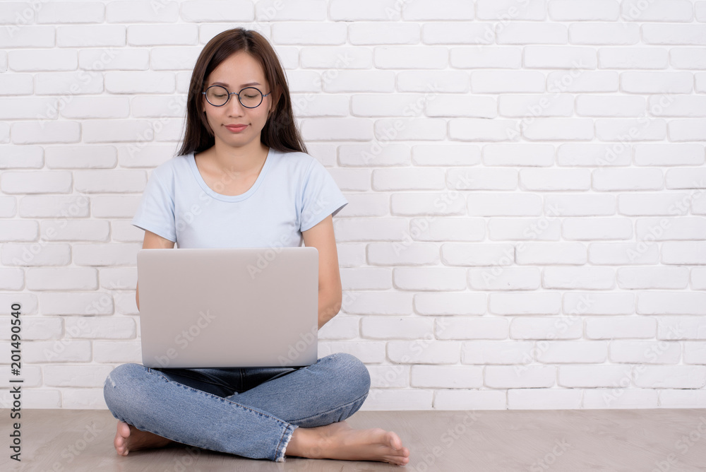 Beautiful young woman in casual wear is using a laptop and smiling, sitting against white brick wall. Portrait of young asian woman working and using laptop computer outdoor on isolated bric. Beautiful young woman in casual wear is using a laptop and smiling, sitting against white brick wall. Portrait of young asian woman working and using laptop computer outdoor on isolated bric.